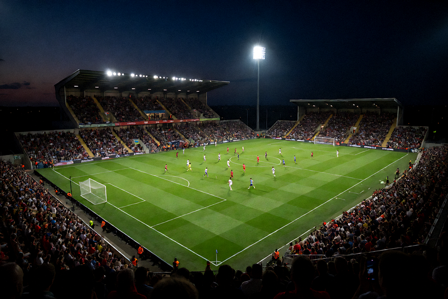 夜晚灯光下的足球场正在进行激烈比赛，观众席灯火通明